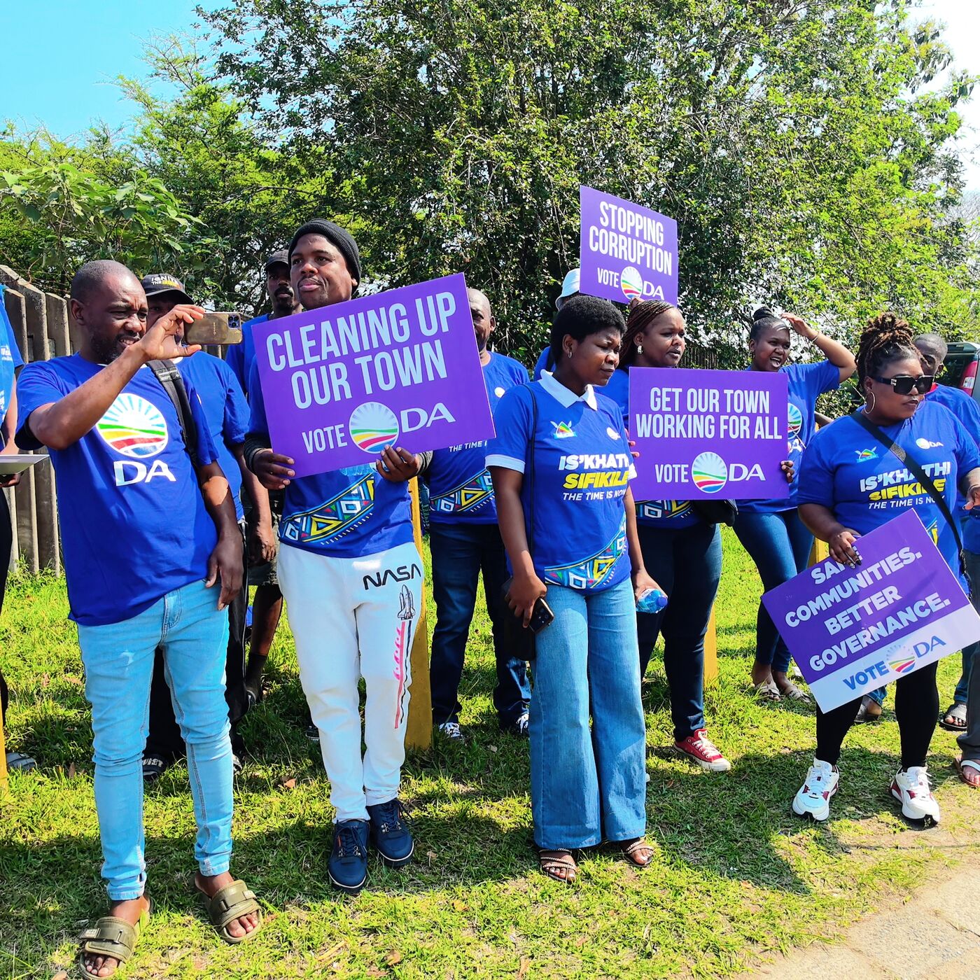 DA supporters holding signs including 'Cleaning Up Our Town' and 'Stopping Corruption'