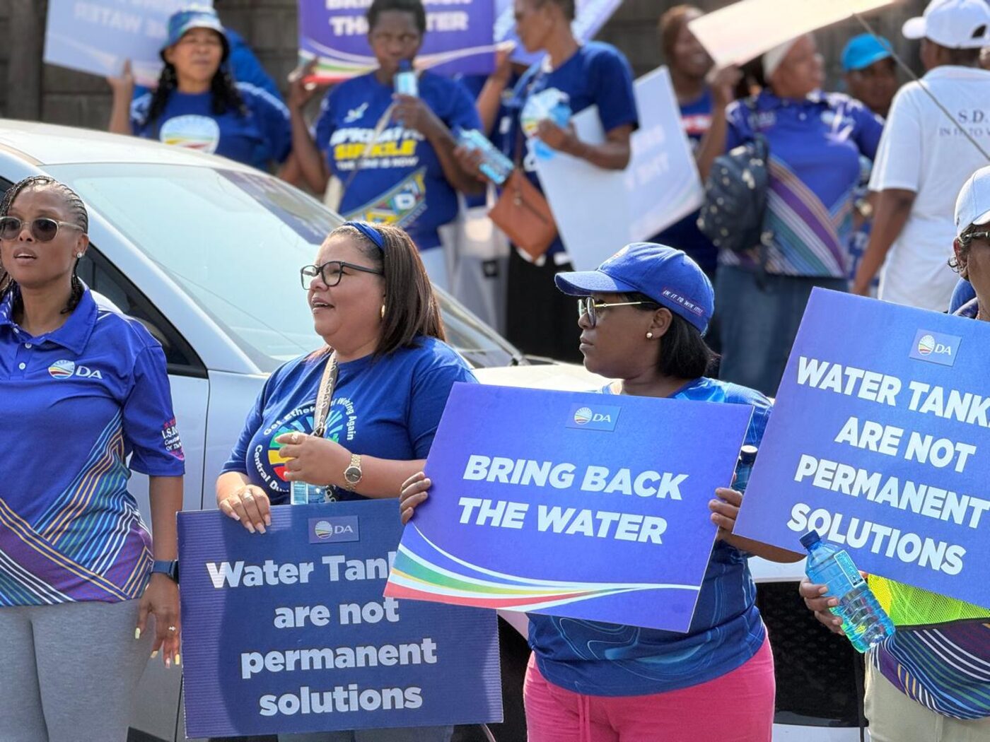 DA supporters holding signs reading 'Bring Back The Water' and 'Water Tankers Are Not Permanent Solutions'