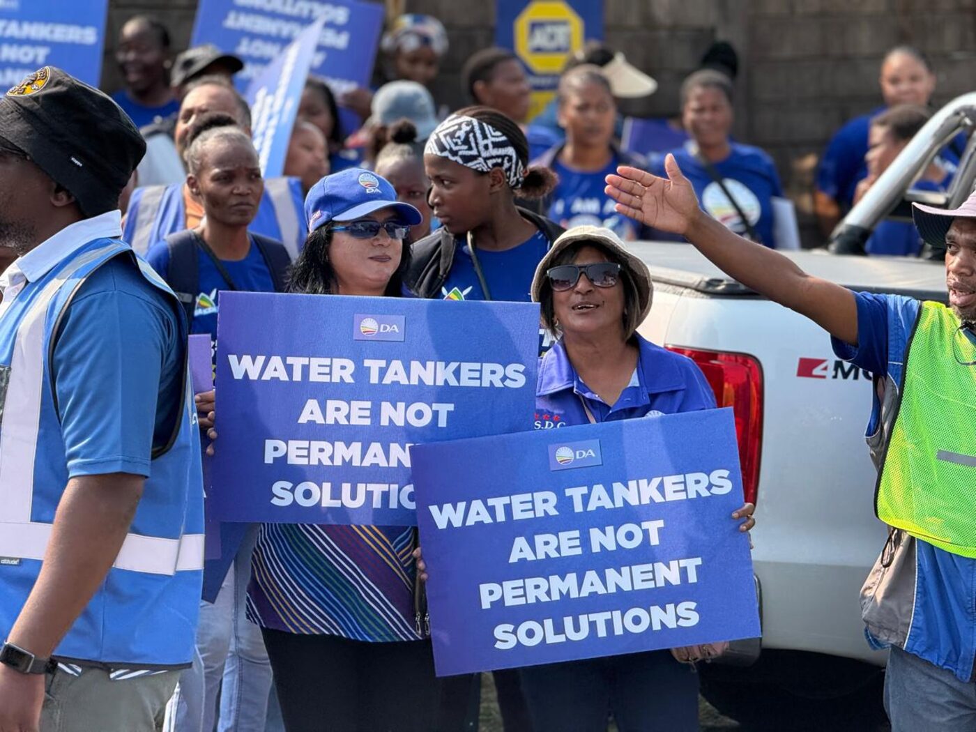 Crowd of DA supporters holding 'Water Tankers Are Not Permanent Solutions' signs